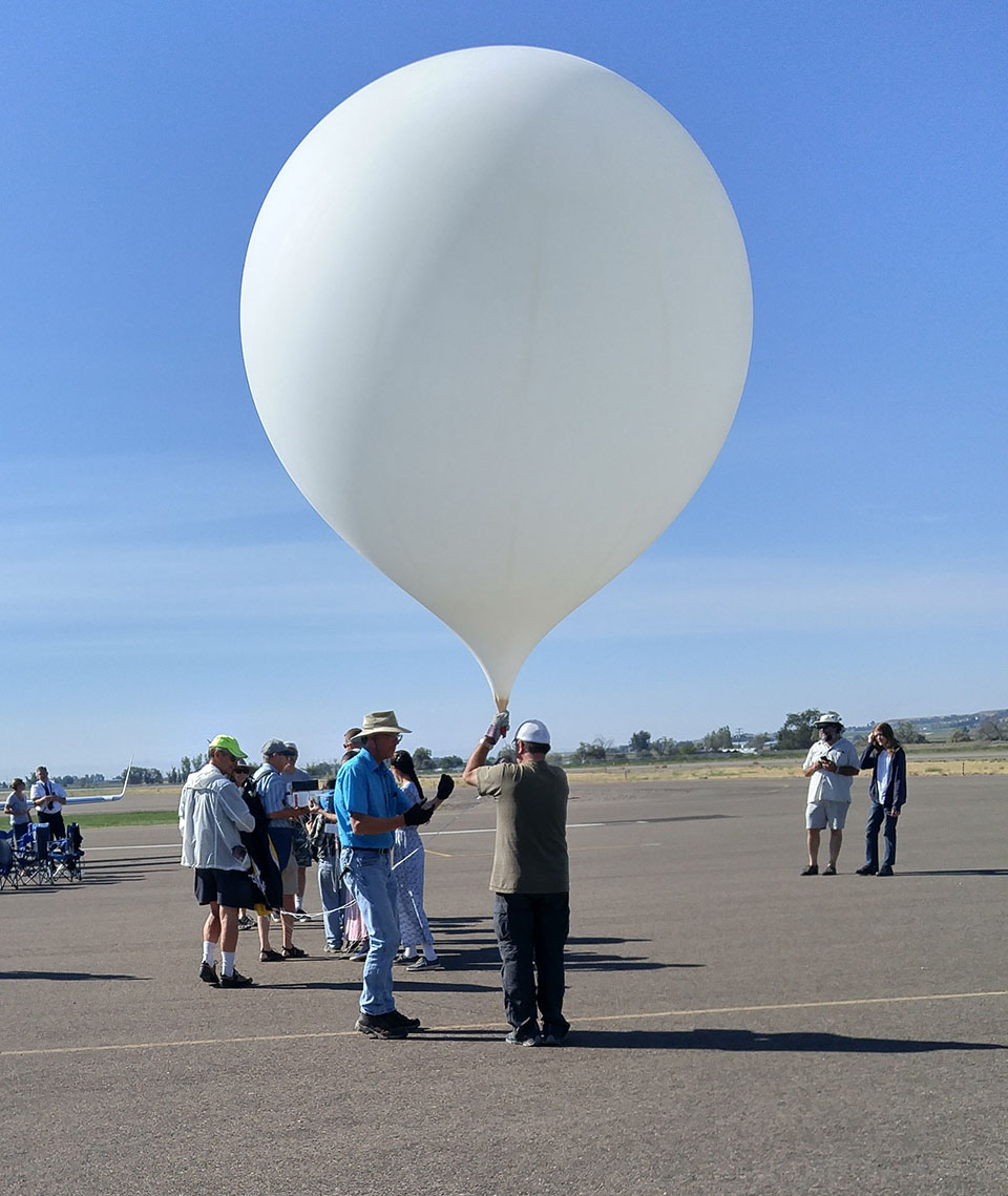 Weather balloons are big. This one was seven feet tall once filled with enough gas to lift its 12 pound science payload. Over half a dozen volunteers, visiting the airport to watch the eclipse, helped get this flight underway.