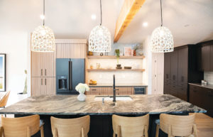 Oversized pendants with an open-weave pattern complement a leathered amazon granite slab on the island in this Bend kitchen.