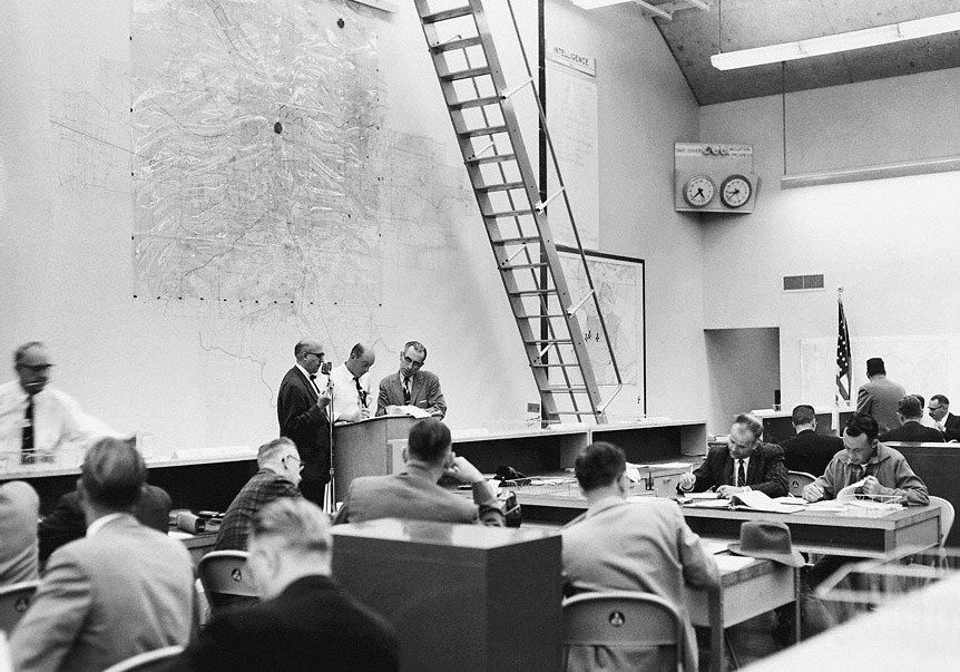 City oﬃcials in the Operations Room of the Civil Defense Center. The center dot on the wall map of Portland marks the primary bomb target area.