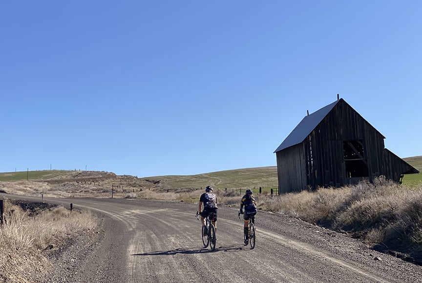 Cyclists pedal past an old farm building along the route.