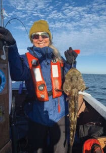 Women fishing in Oregon with a big catch of a flatfish, ocean sky, and boat, highlighting Oregon outdoor recreation and fishing culture.