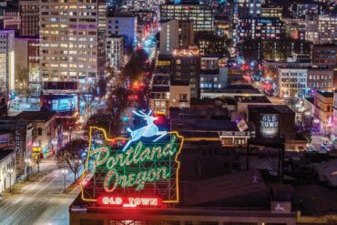 Brightly lit Portland cityscape with downtown buildings and neon "Old Town" sign at night, showcasing vibrant urban life and city lights, capturing the essence of Portland, Oregon.
