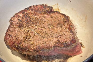 Prime rib roast seasoned with herbs and spices, cooking in a skillet.