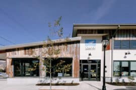 Modern coworking space with a wooden exterior, large windows, and outdoor seating, designed to foster talent and innovation in a collaborative environment.
