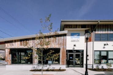 Modern coworking space with a wooden exterior, large windows, and outdoor seating, designed to foster talent and innovation in a collaborative environment.