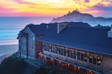 Beautiful view of Headlands Coastal Lodge & Spa overlooking the ocean at sunset, with a scenic island in the background, showcasing Oregon’s stunning coastal landscape.