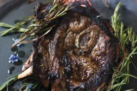 Juicy roasted lamb leg garnished with fresh rosemary and edible flowers, served on a black platter. Perfect for gourmet dining and special occasions.