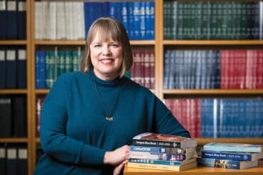Woman smiling in a library with stacks of Oregon Blue Books, representing Oregon's literary and historical stories.