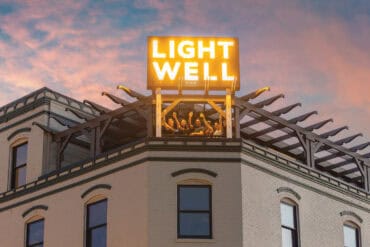 Exterior view of the Lightwell Hotel & Spa with illuminated sign on rooftop during sunset, showcasing the building's architecture and vibrant evening atmosphere.