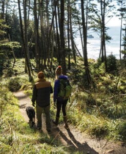 Enjoying a scenic hike through lush forest near the Oregon coast with friends and a dog, promoting outdoor wellness and a healthier, happier lifestyle at Haystack.