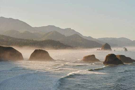 Oregon coast landscape featuring rocky formations, ocean waves, and misty mountains, highlighting natural beauty and outdoor serenity in Oregon.