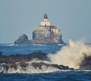 Seaside lighthouse perched on a rocky island with ocean waves crashing against the shore, symbolizing coastal beauty and maritime safety in Oregon.