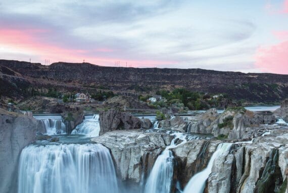 A scenic view of powerful waterfalls in Daredevil Country, Oregon, during sunset, showcasing rugged terrain, cascading water, and dramatic natural beauty.